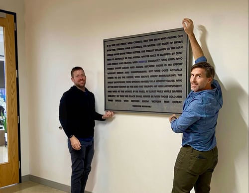 Striveworks team member hanging meaningful 'man in the arena' quote in HQ lobby